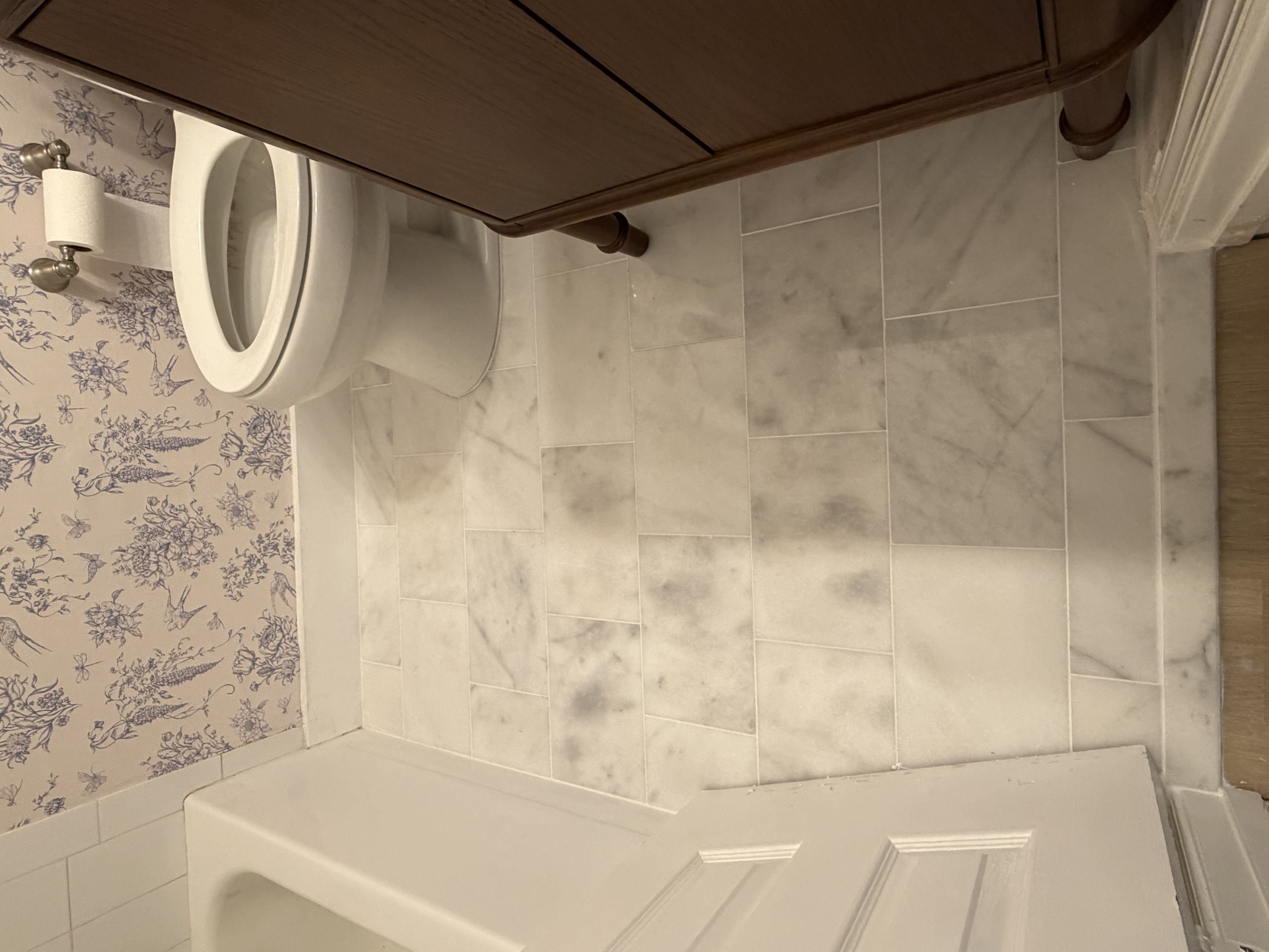 Finished bathroom tile installed around the toilet and vanity with a clean marble-look pattern