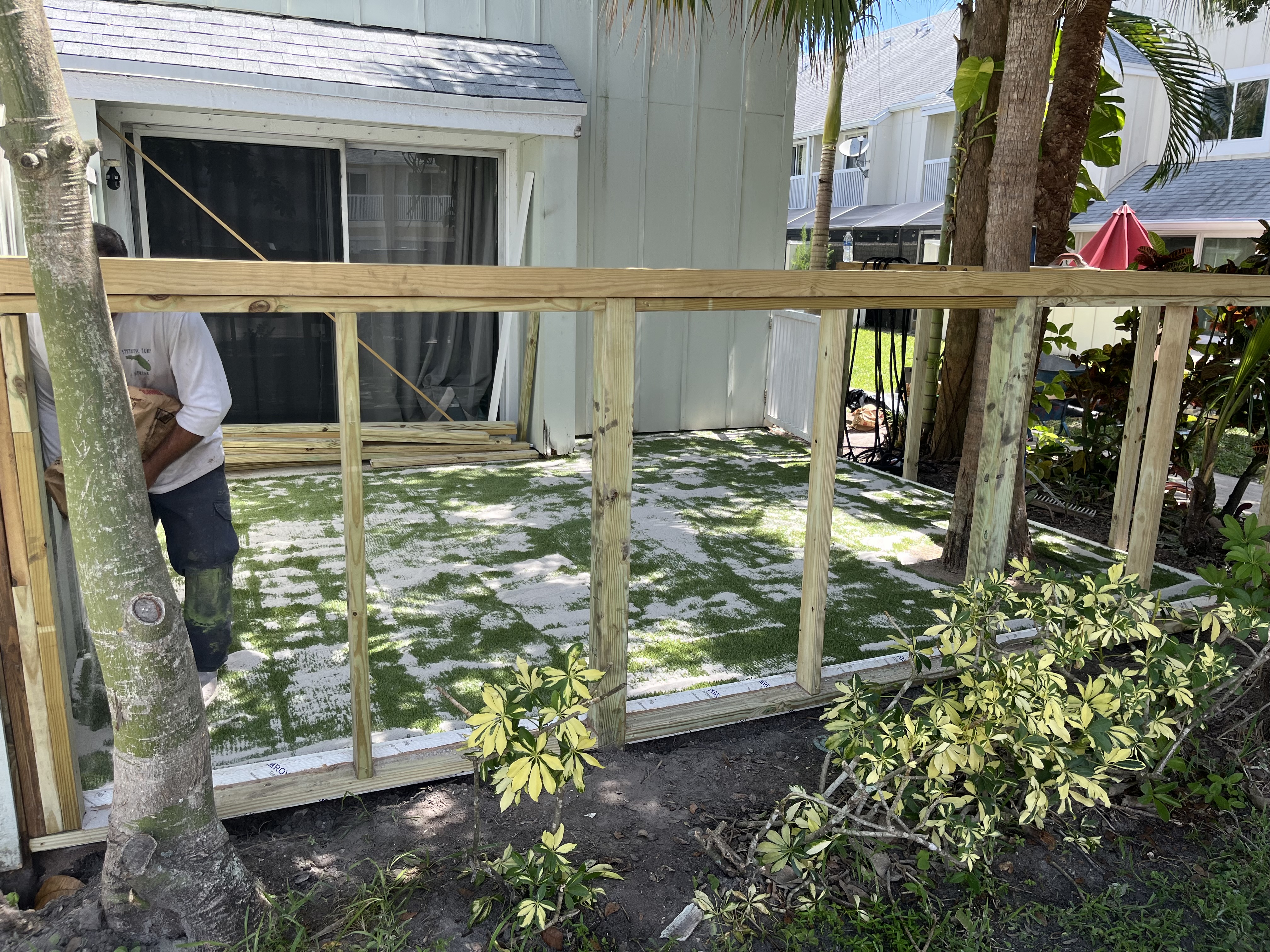 Artificial turf laid across the backyard during installation with the new fence framing in place