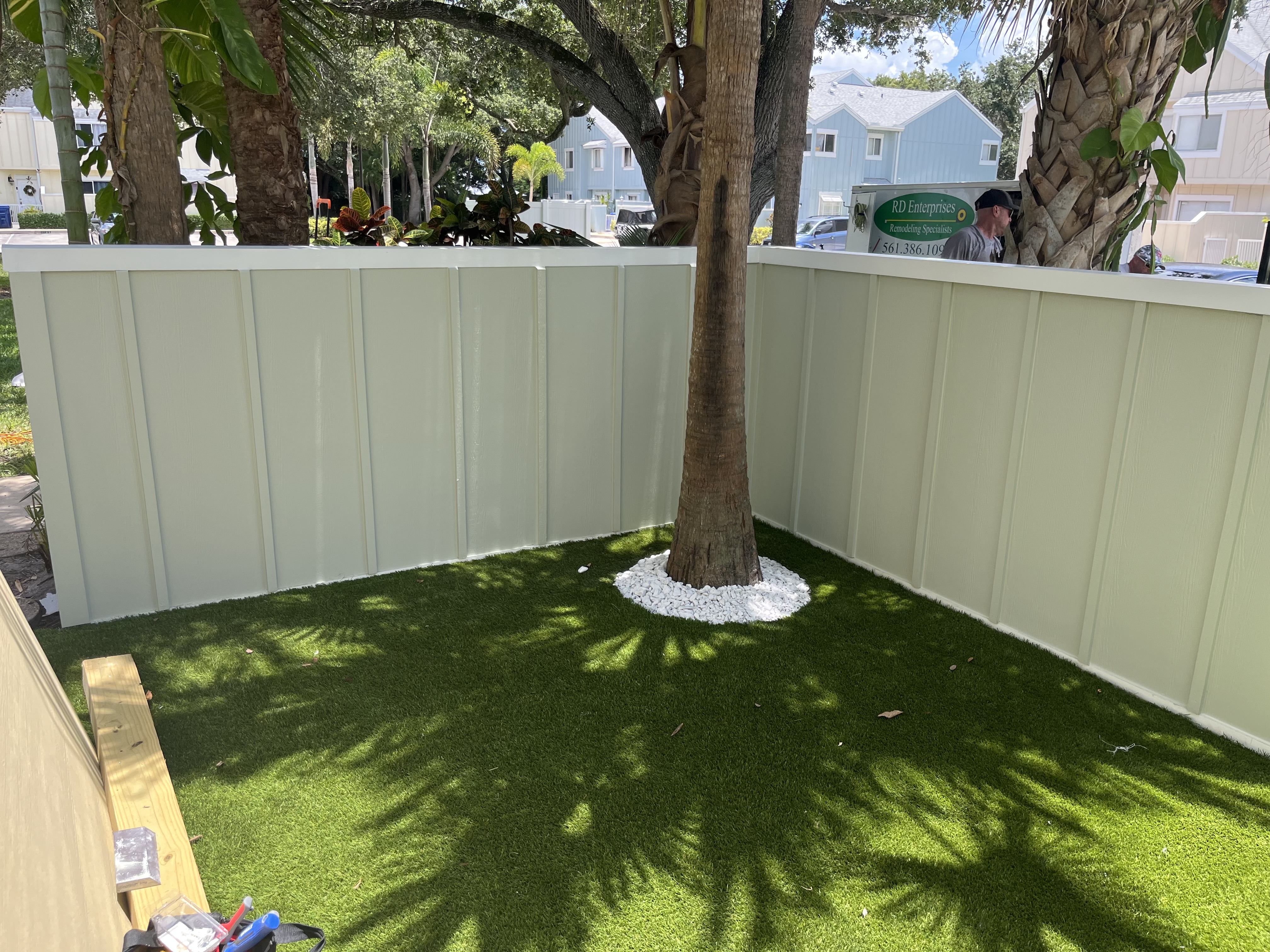 Completed backyard with new fence panels, fresh trim, and artificial turf around the tree