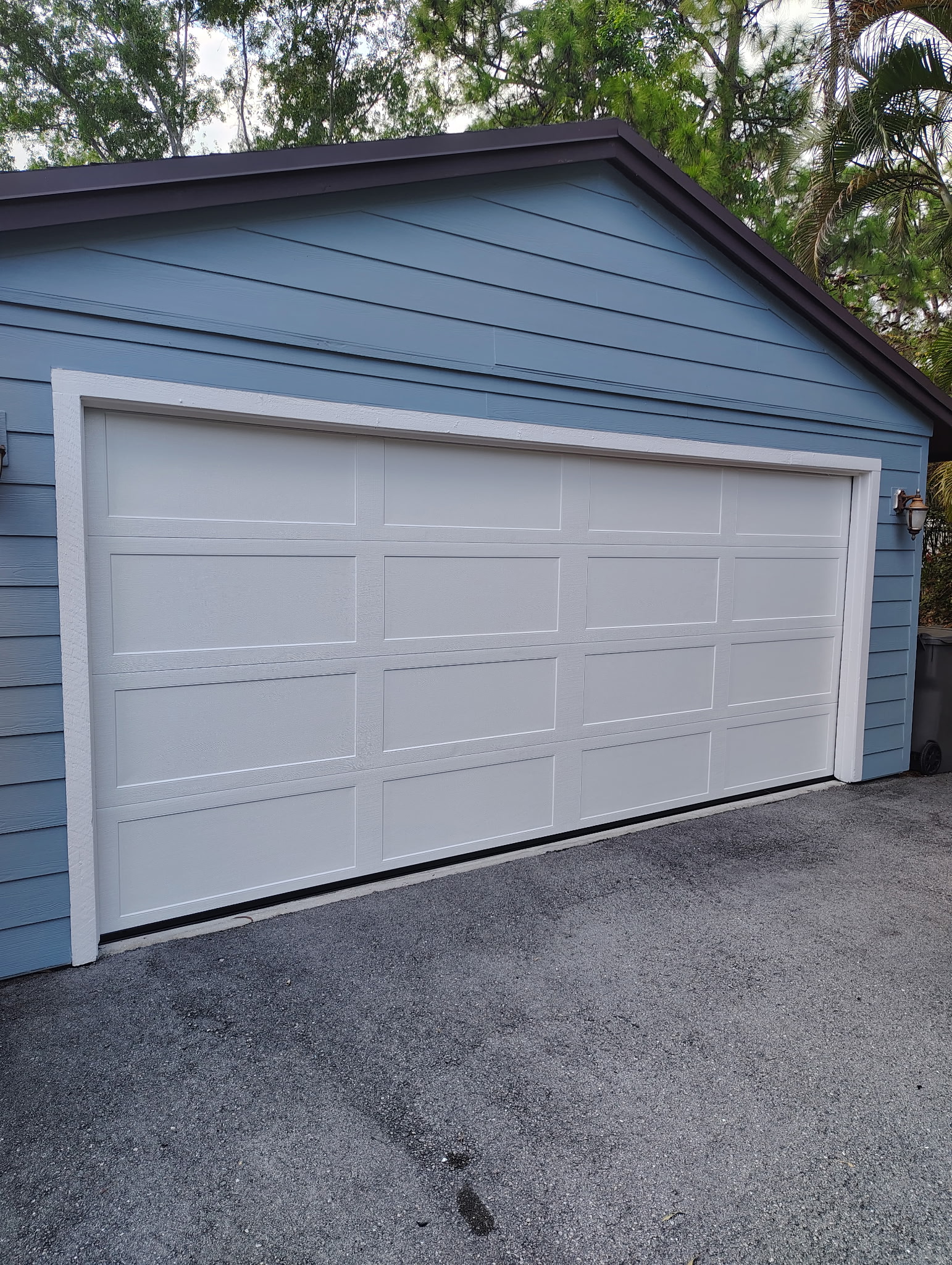 Finished white garage door installed on a blue detached garage with fresh white trim