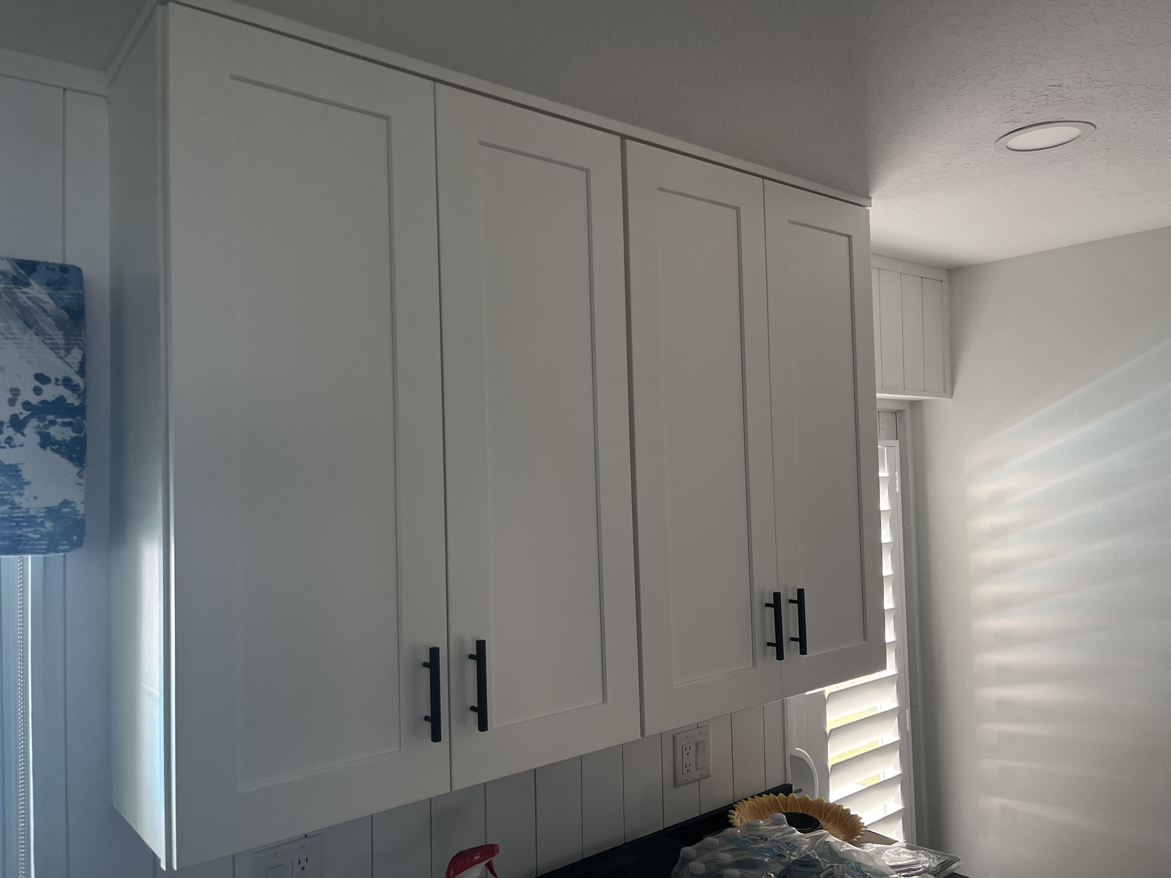 Finished run of tall white kitchen cabinets installed beside a window with black hardware