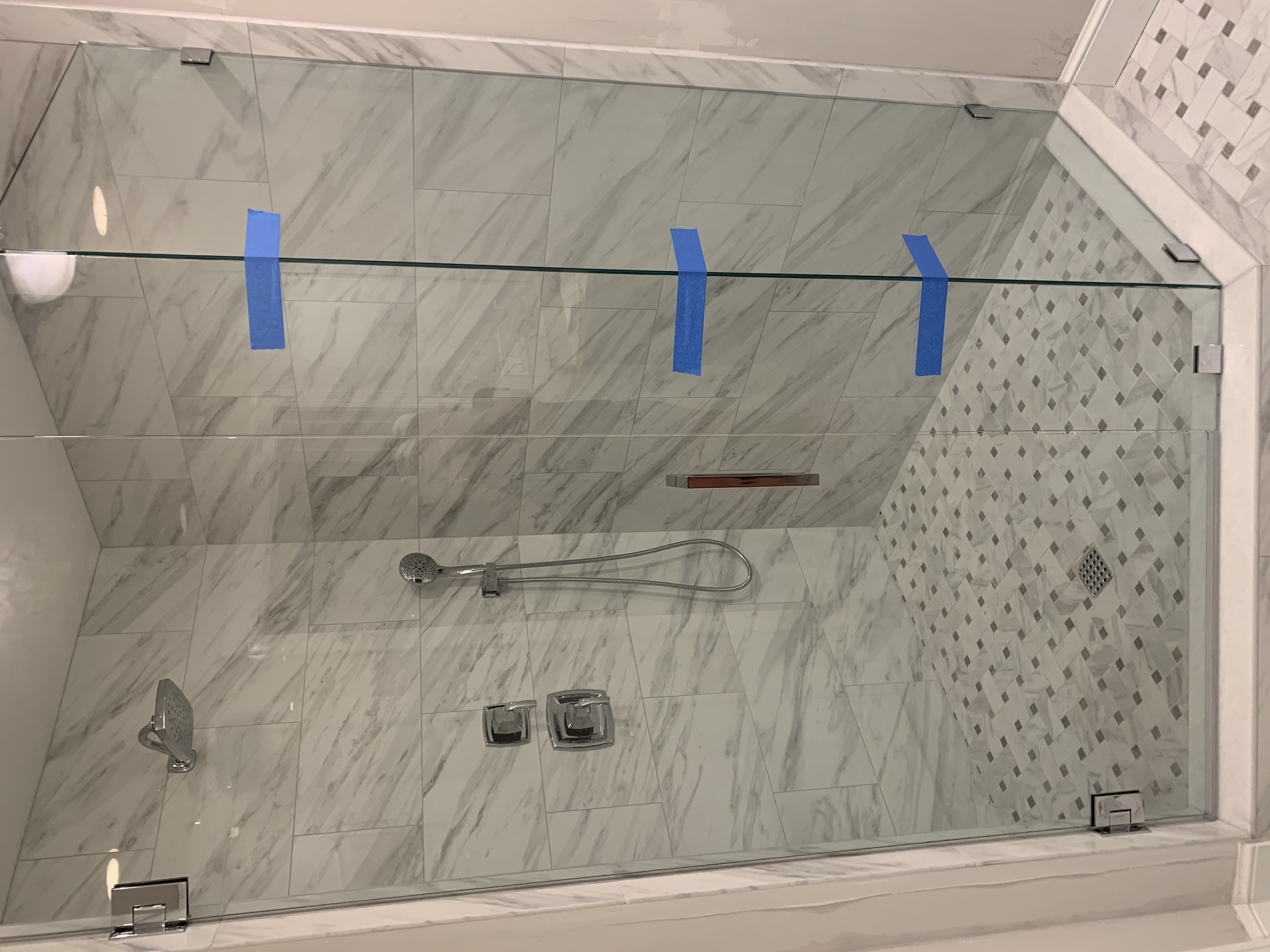 Finished shower with marble-look tile, mosaic floor, and glass enclosure